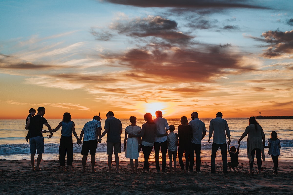 Three generations of a family standing together on a beach at sunset