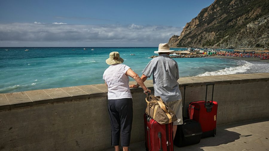 A retired couple with suitcases looking at the sea